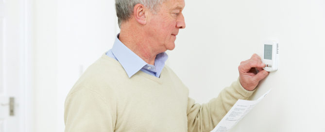 Worried Senior Man With Bill Turning Down Heating Thermostat