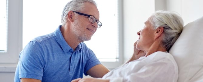 older man comforting an older woman in a hospital bed