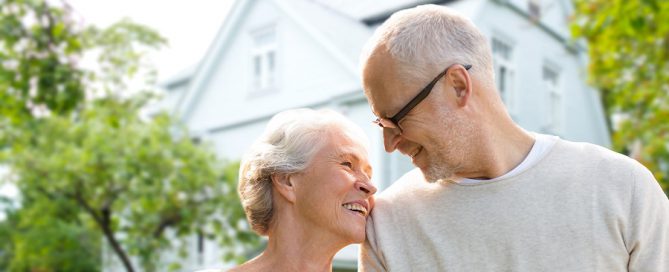 age in place happy older couple with large house behind them