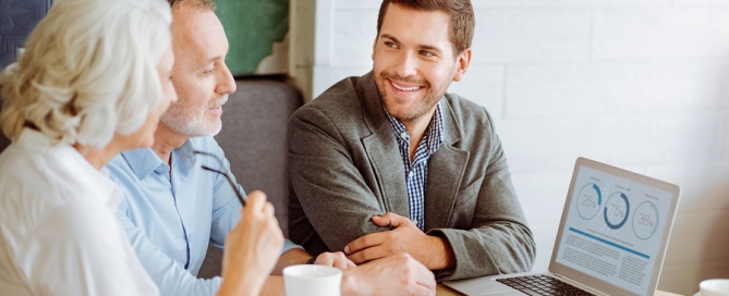 sales counselor talking with senior couple, looking at a laptop long-term care