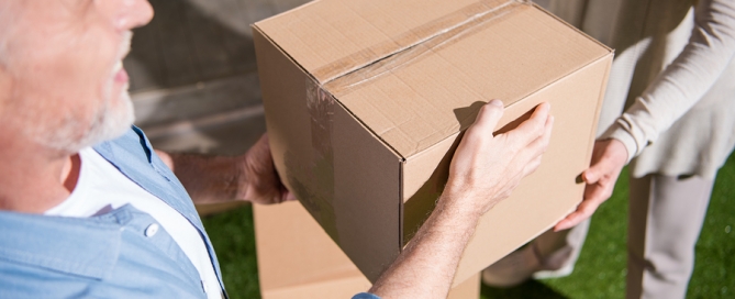 senior couple holding cardboard box while moving into new house