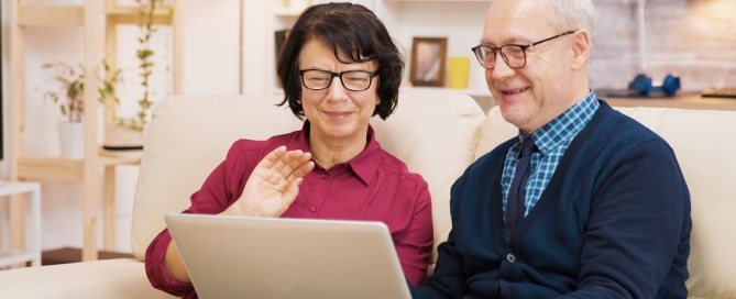 resiliency senior living Elderly Age Couple Sitting On Sofa Holding Laptop During A Video