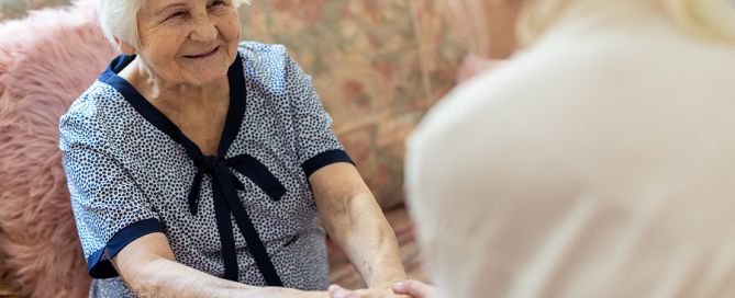 Female caregiver supporting old woman to stand up from the sofa family caregiving stress