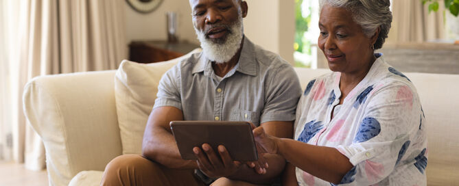 Senior African American couple sitting on sofa using tablet CCRC website