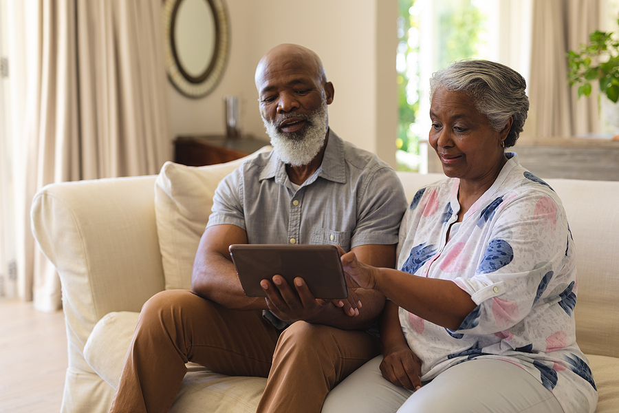 Senior African American couple sitting on sofa using tablet CCRC website