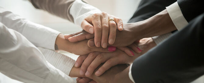 Diverse people putting stacked hands together DEIB CCRC senior living