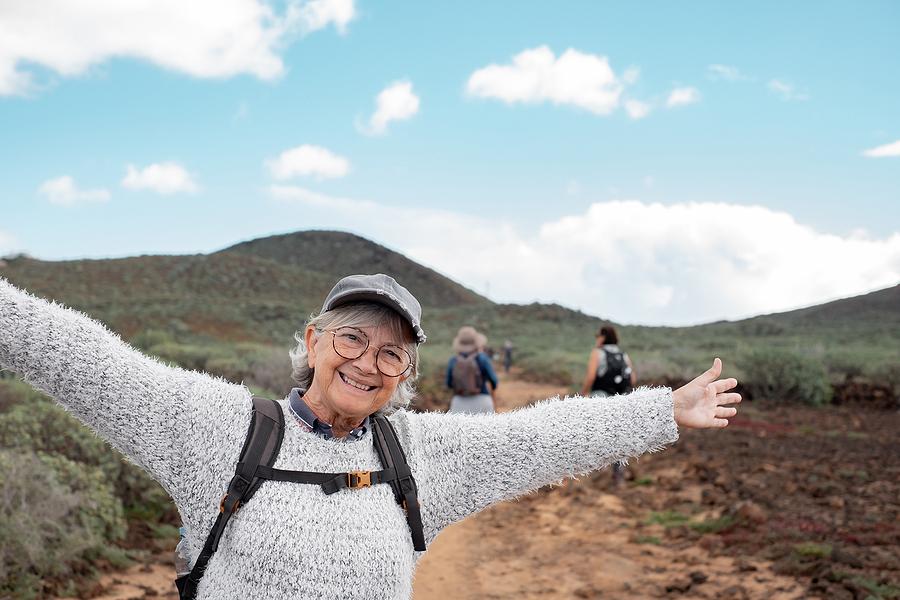 Senior Happy Woman With Backpack Walking In Countryside Footpath secret to healthy aging reverse aging