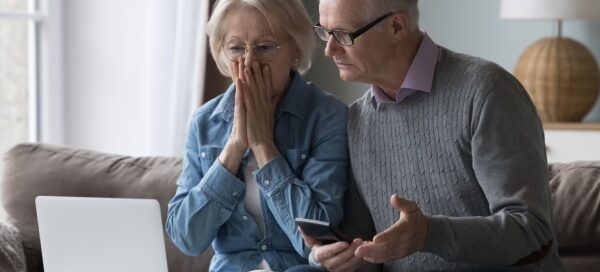 elder fraud; older adult couple looking with shock at laptop and phone