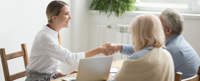 young professional woman shaking hands at table with senior couple; senior living sales success
